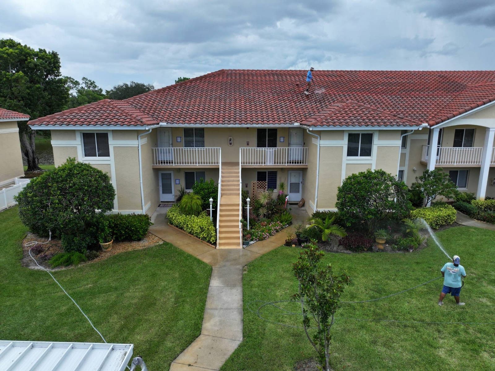Drone view of the Dolphin crew washing a red tile condo roof in Naples, one on the roof and one rinsing the landscaping