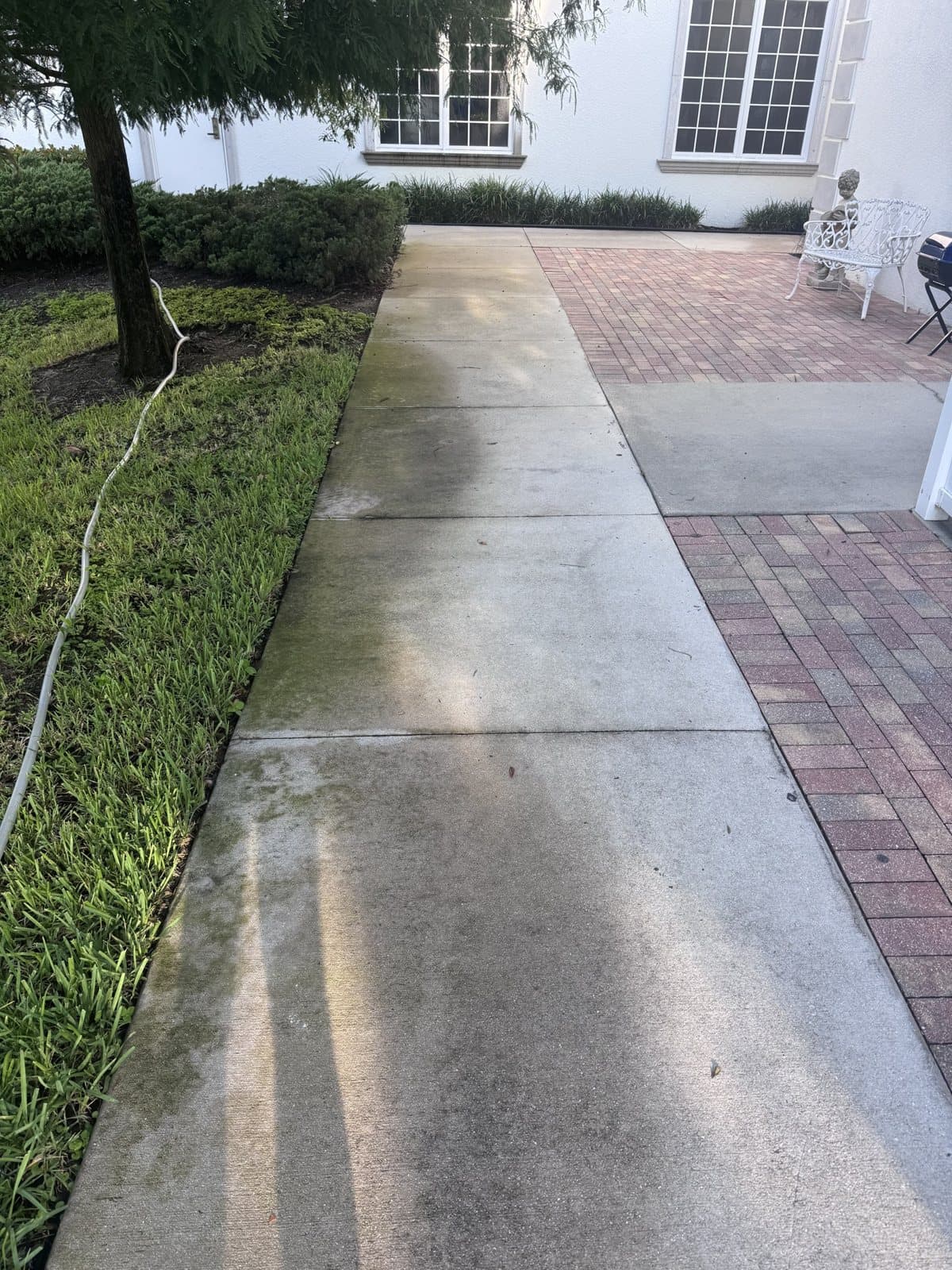 Concrete walkway half pressure washed beside a paver driveway in Naples