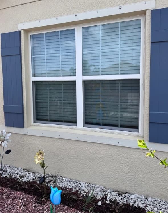 Clean double hung window between blue shutters on a stucco home in Naples